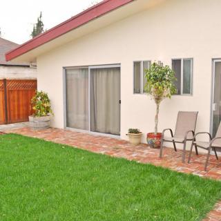 A backyard featuring a green lawn, patio chairs, potted plants, and sliding glass doors.