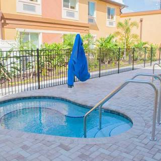 A cozy outdoor jacuzzi with a paved deck, surrounded by a secure fence and overlooked by an apartment building.