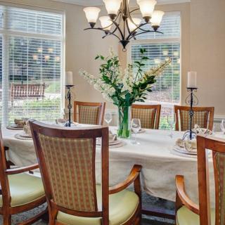 A well-lit dining room with a set table, elegant chairs, and a floral centerpiece.