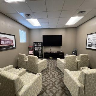 A cozy room with arranged chairs facing a television, decorated with wall art and carpet flooring.