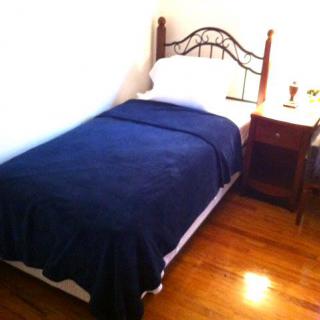 A minimalist bedroom featuring a single bed with a blue blanket and a wooden nightstand.