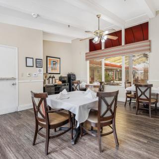 A cozy dining area with neatly arranged tables and chairs, featuring large windows and warm decor.