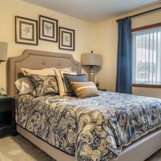 A cozy bedroom with elegant bedding, artwork on the wall, and a window with blue curtains.