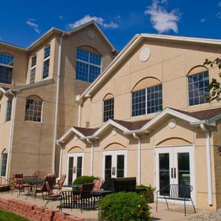 A sunny day view of a residential building with large windows and outdoor seating.