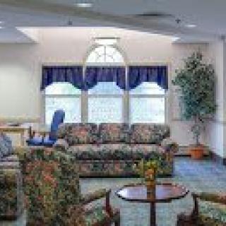 A cozy living room featuring floral-patterned furniture, a coffee table, and large windows with blue curtains.