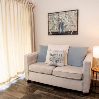 A cozy living room with a beige sofa, decorative cushions, wall art, and soft lighting.