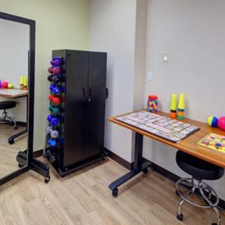 A well-organized workspace featuring a mirror, storage cabinet with dumbbells, and a desk with chairs.