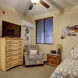 Cozy bedroom with patterned armchair, wooden dresser, and a TV.