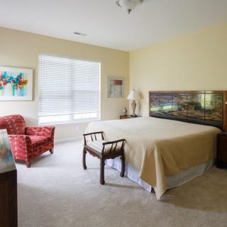 A cozy bedroom with a large bed, upholstered chairs, and vibrant artwork on the walls.