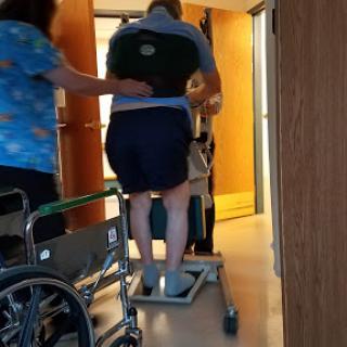 A healthcare worker assists a patient in a transfer using a mobility aid in a hospital setting.