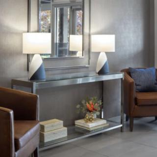 A modern lounge area with a metallic console table, adorned with lamps, books, and a vase of flowers, placed in front of a large wall mirror.