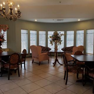 A well-furnished room with tables, chairs, a chandelier, and large windows.