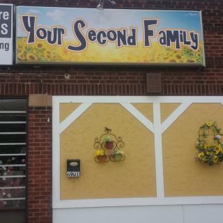 A storefront with a sign reading 'Your Second Family' above a yellow and brick exterior adorned with flower arrangements.