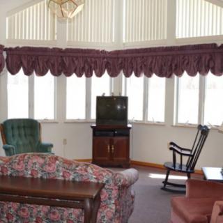 A cozy living room with a couch, armchair, rocking chair, and TV set against a wall of windows with valance curtains.