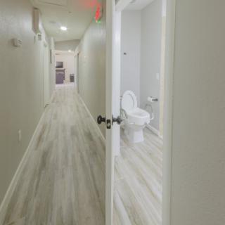 A hallway with an open door leading to a bathroom, featuring modern flooring and lighting.