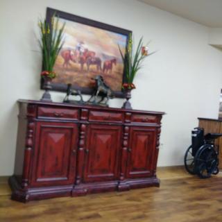 A wooden cabinet with decorative plants and artwork, next to a wheelchair in a room.
