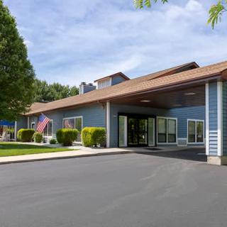 A building with a covered entrance and an American flag, surrounded by trees, under a clear sky.