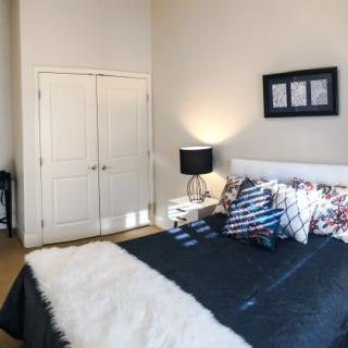 A modern bedroom with stylish decor, featuring a bed with decorative pillows, a lamp on a side table, and artwork above the headboard.