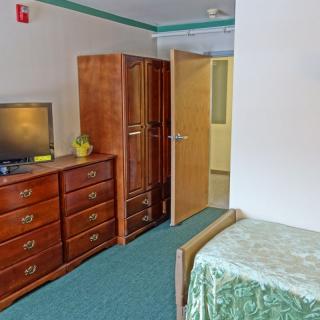 A cozy bedroom with wooden furniture, including a wardrobe, dresser, and a television.