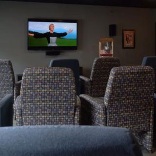 A cozy home theater setup with empty chairs facing a screen displaying an animated scene, complemented by a popcorn machine in the background.