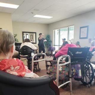 A group of elderly individuals seated in a nursing home during an indoor community event.