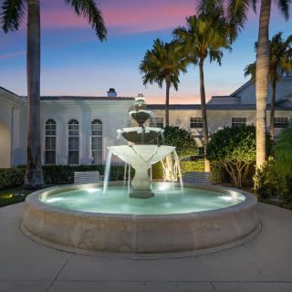 A beautifully lit fountain surrounded by palm trees in an outdoor setting at sunset.