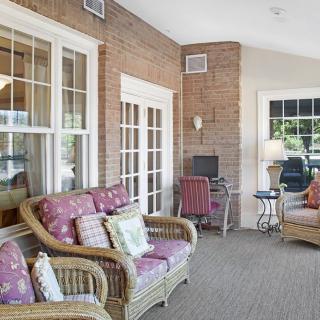 A cozy sunroom featuring wicker furniture, large windows, and a carpeted floor.