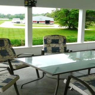 An outdoor patio with a glass table and chairs, overlooking a countryside landscape.