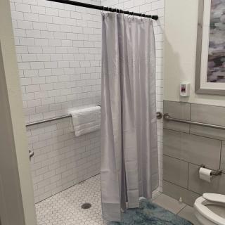 A modern bathroom with a shower, white tiles, and a blue bath mat.