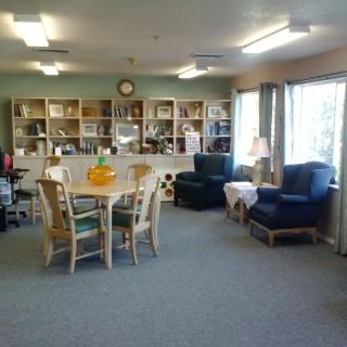 A cozy living room with a table and chairs, surrounded by bookshelves and armchairs.