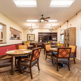 A well-lit dining area with wooden tables, upholstered chairs, and a ceiling fan.