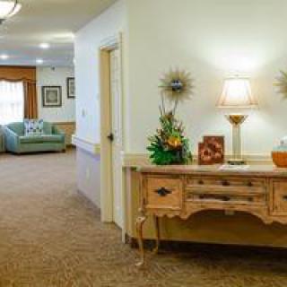 A well-decorated hallway with a wooden console table, lamp, and floral arrangement, leading to a cozy living room area.