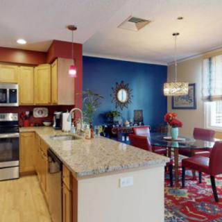 A modern kitchen and dining area with an open concept design featuring a spacious island, stainless steel appliances, and vibrant color accents.