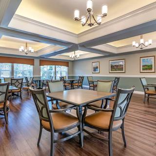 A spacious and well-lit dining area with multiple tables and chairs, complemented by elegant chandeliers and large windows.