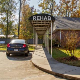 The entrance to a rehab facility with a car parked in front, featuring an awning labeled 'REHAB'.