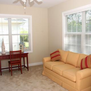 A cozy living room with a yellow sofa, desk, and chair by the window.