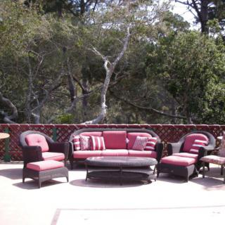 A cozy outdoor seating area with red and black upholstered furniture on a spacious deck surrounded by trees.
