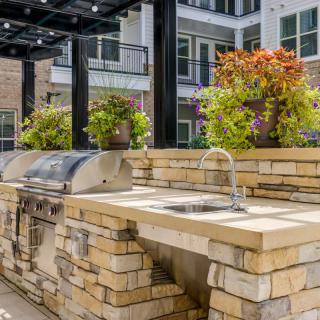 A modern outdoor kitchen area with a grill and sink, adorned with vibrant potted plants under a pergola.