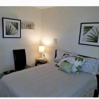 A cozy bedroom with simple decor, featuring a neatly made bed, a bedside lamp, and framed leaf artwork on the walls.