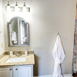 A well-lit bathroom features a mirror above a granite countertop with a towel hanging on the wall.