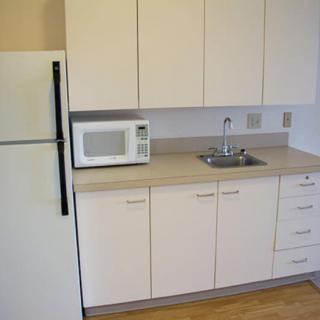 A small kitchen area with a refrigerator, microwave, sink, and cabinets.