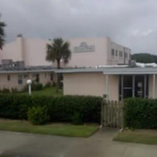 A school building with a palm tree nearby on a cloudy day.