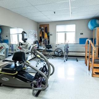 A well-lit fitness room equipped with various exercise machines and rehabilitation equipment.