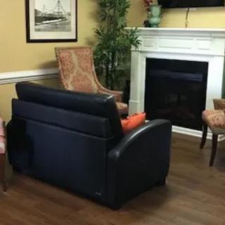 A cozy living room with a black sofa and chairs arranged around a fireplace.