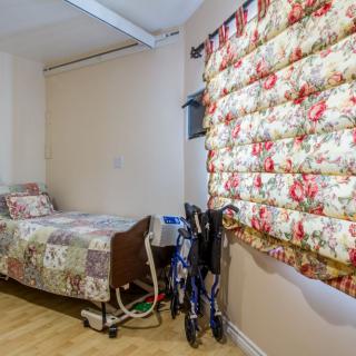 A cozy room featuring a single hospital bed with floral bedding, a matching floral curtain, and a wheelchair.
