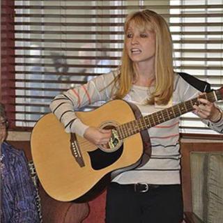 A person playing an acoustic guitar indoors, possibly during a live performance.
