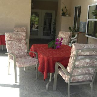 A cozy patio setup with a table covered in a red tablecloth, surrounded by cushioned chairs and adorned with potted plants.
