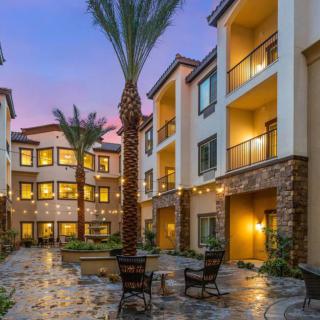 A beautifully lit apartment complex courtyard at dusk, featuring palm trees and outdoor seating.