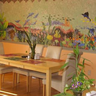 A colorful dining room featuring a vibrant wall mural with plants and a wooden table set.