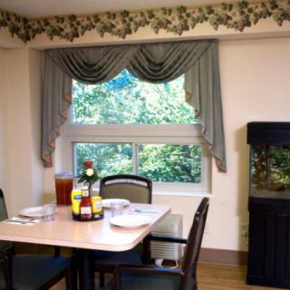 A cozy dining room with a table set for four, featuring elegant curtains and a fish tank by the window.